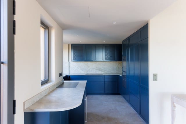 Perspective pièce à vivre : arcs enduits, poutres blanches, cuisine bleue en fond, joints réguliers — rénovation de villa premium DOMTY Construction à Toulon (Cap Brun).