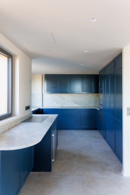 Cuisine sur-mesure bleue, plan de travail minéral arrondi, crédence pierre claire, pose millimétrée — rénovation de villa par DOMTY Construction à La Ciotat.